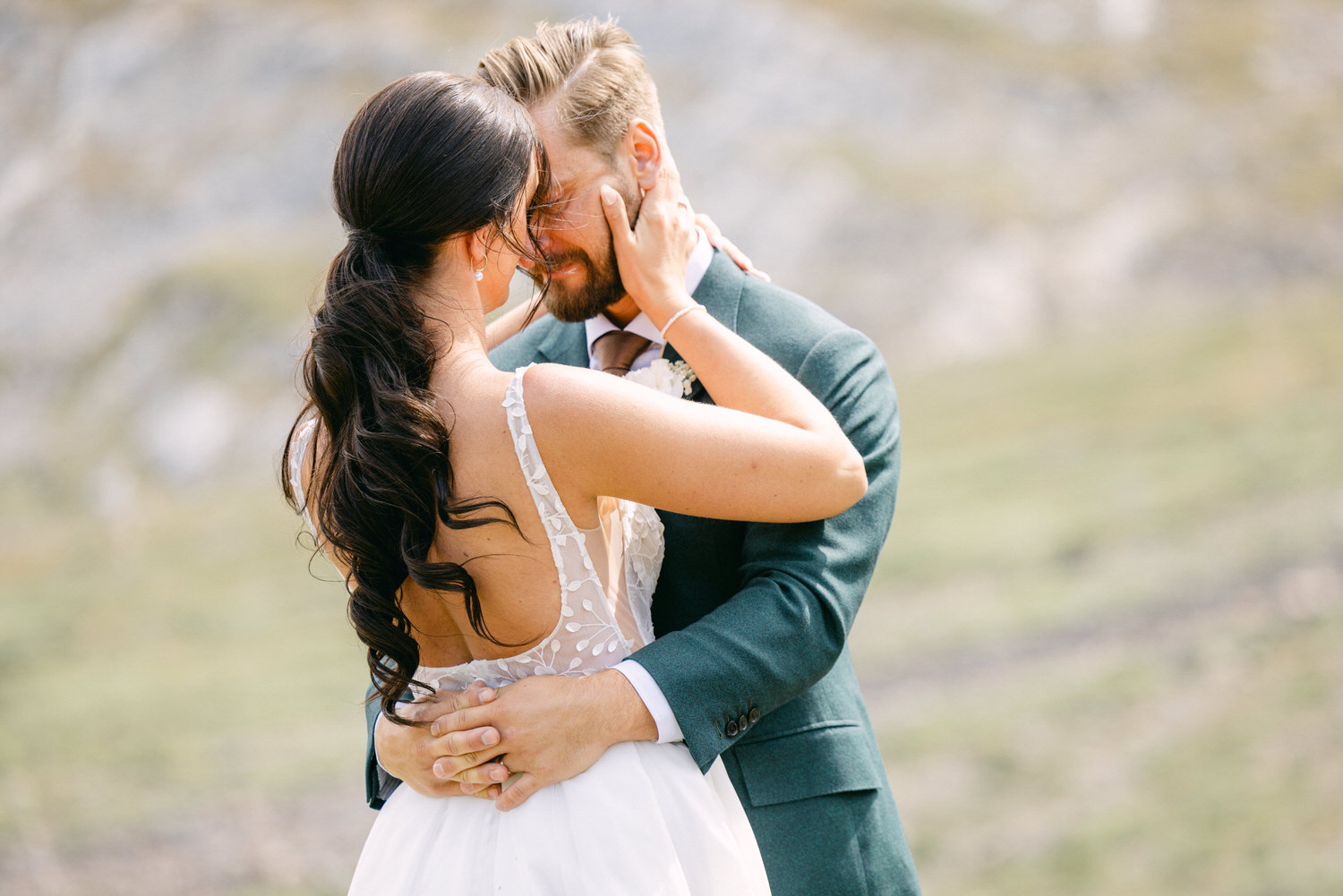 A romantic moment captured between a couple embracing outdoors, showcasing their joy and love, with a blurred natural landscape in the background.