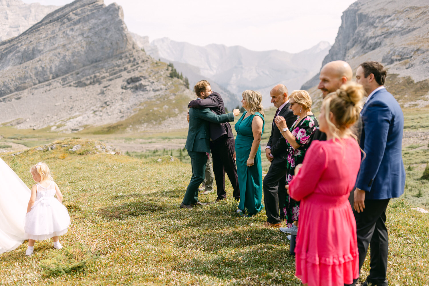 A couple sharing a heartfelt embrace during a wedding ceremony, surrounded by family and friends in a stunning mountainous landscape.