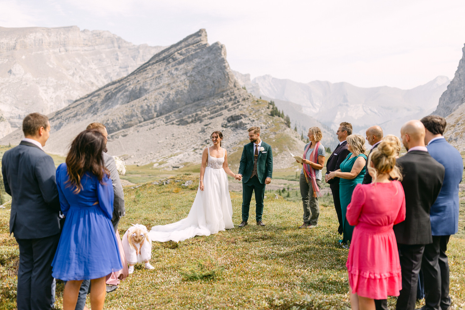 A couple stands hand-in-hand during their wedding ceremony in a picturesque mountain setting, surrounded by friends and family.