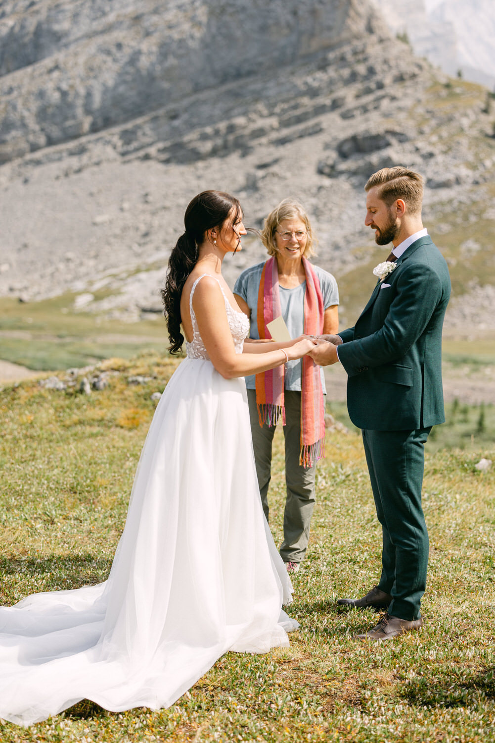 Wedding Ceremony in Nature::A couple exchanging vows outdoors, with a serene mountain landscape in the background and an officiant present.