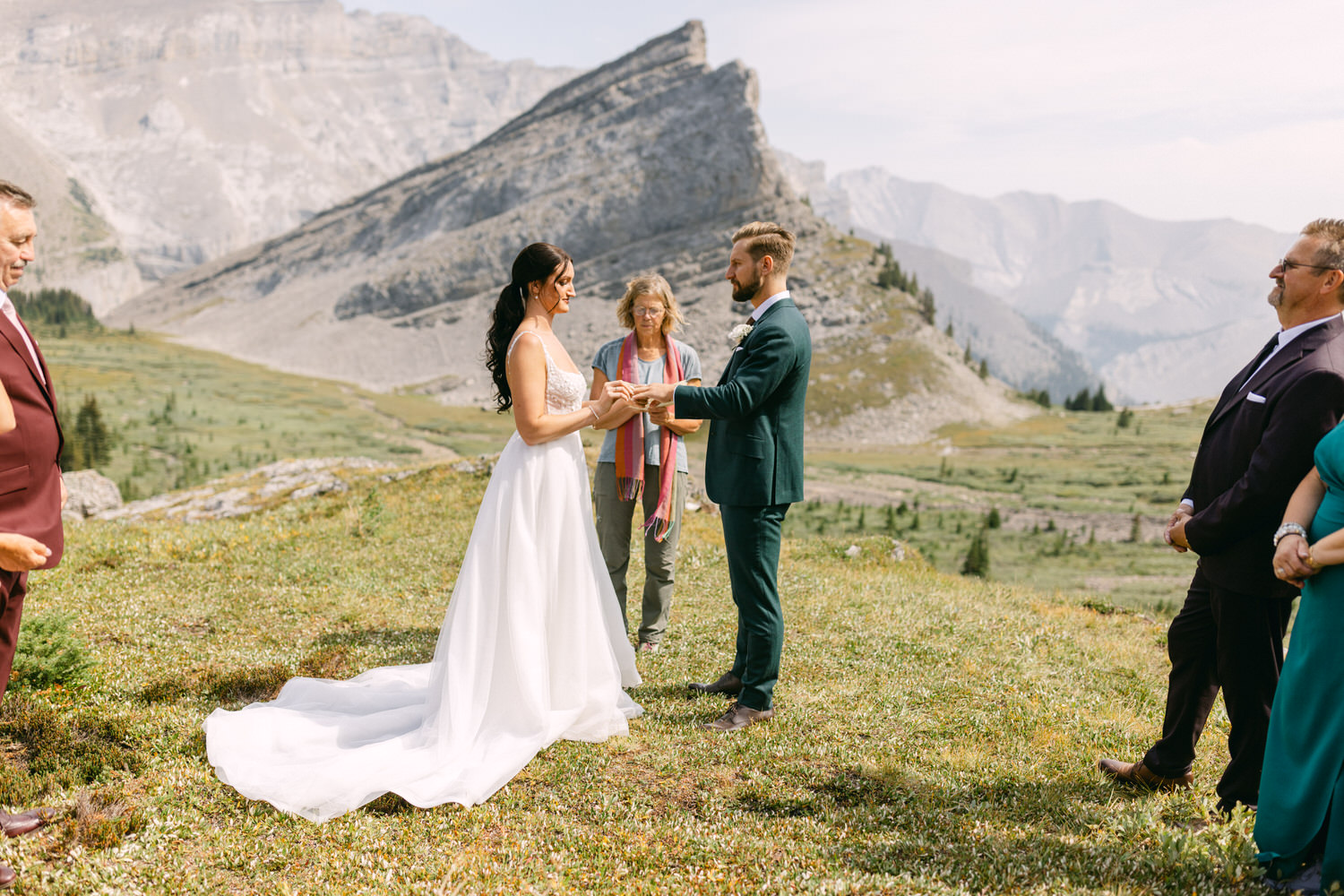 A couple exchanging vows during their wedding ceremony in a stunning mountainous landscape, surrounded by friends and family.