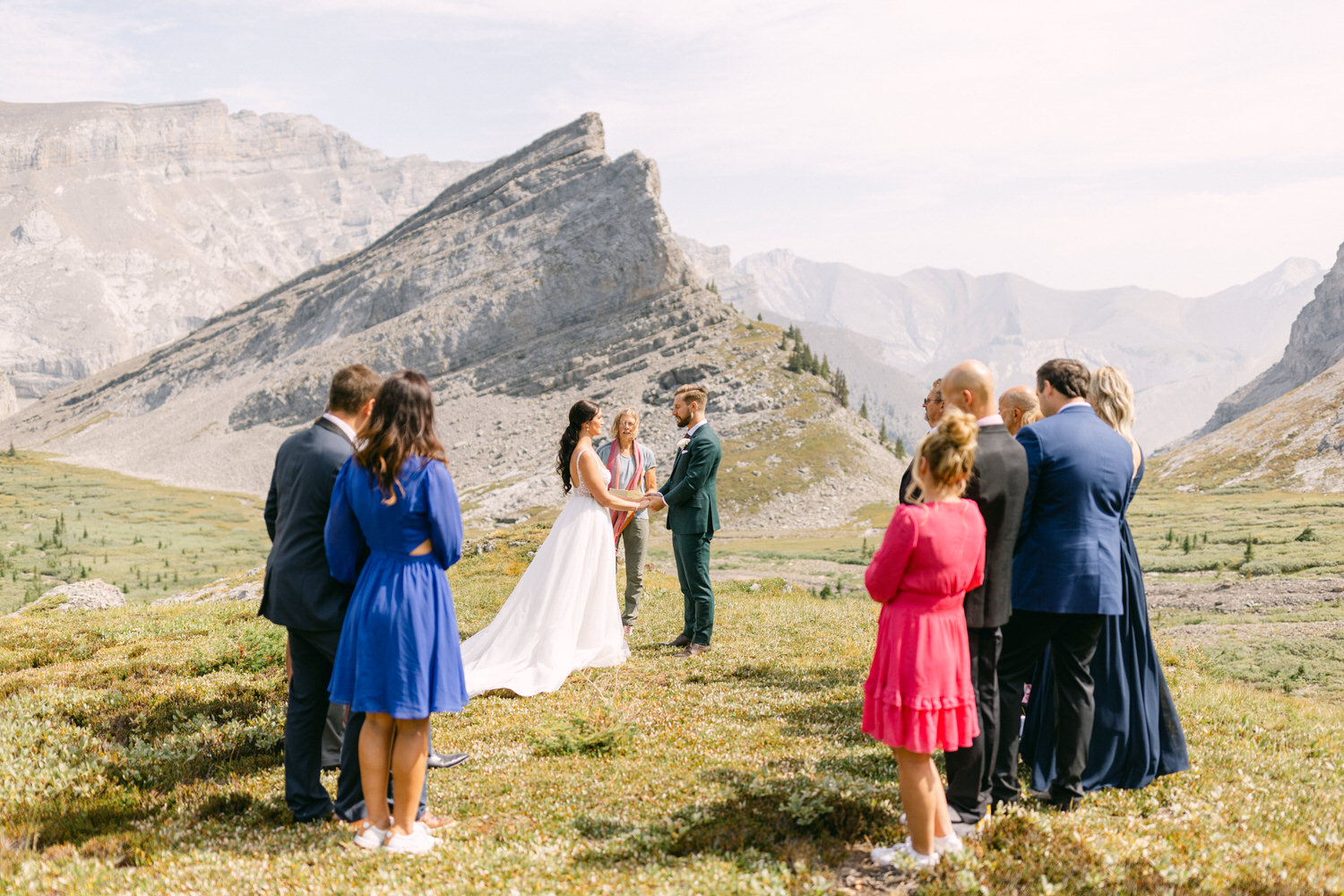 A couple exchanges vows surrounded by friends and family in a scenic mountainous landscape.