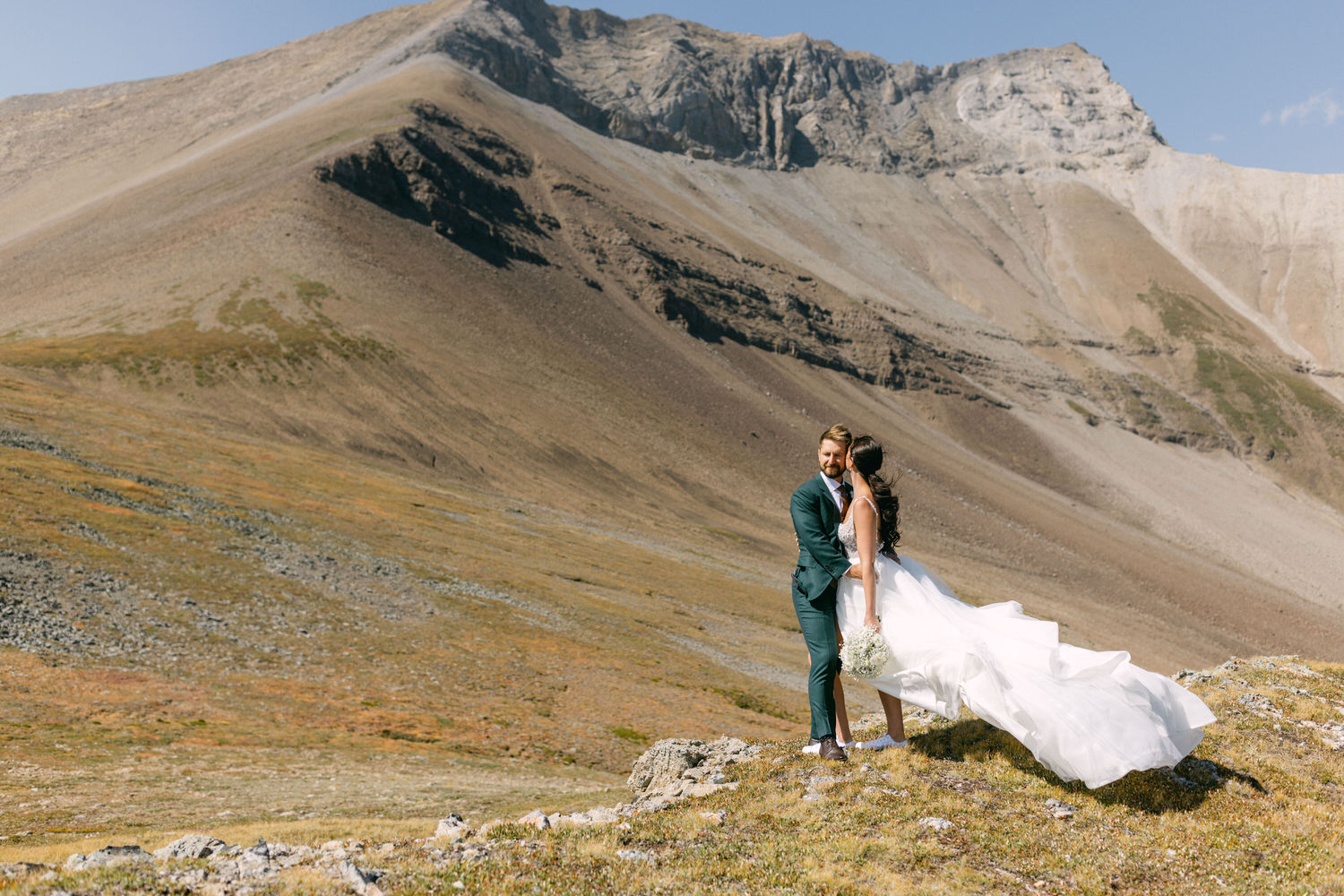 A bride and groom embrace on a rocky, mountainous landscape, showcasing their love against a stunning natural backdrop.