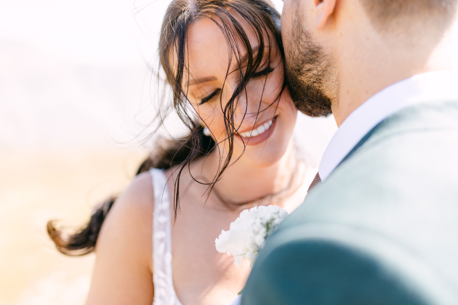 A couple sharing an intimate moment outdoors, with the bride smiling and her hair gently blowing in the wind, while the groom leans in close.