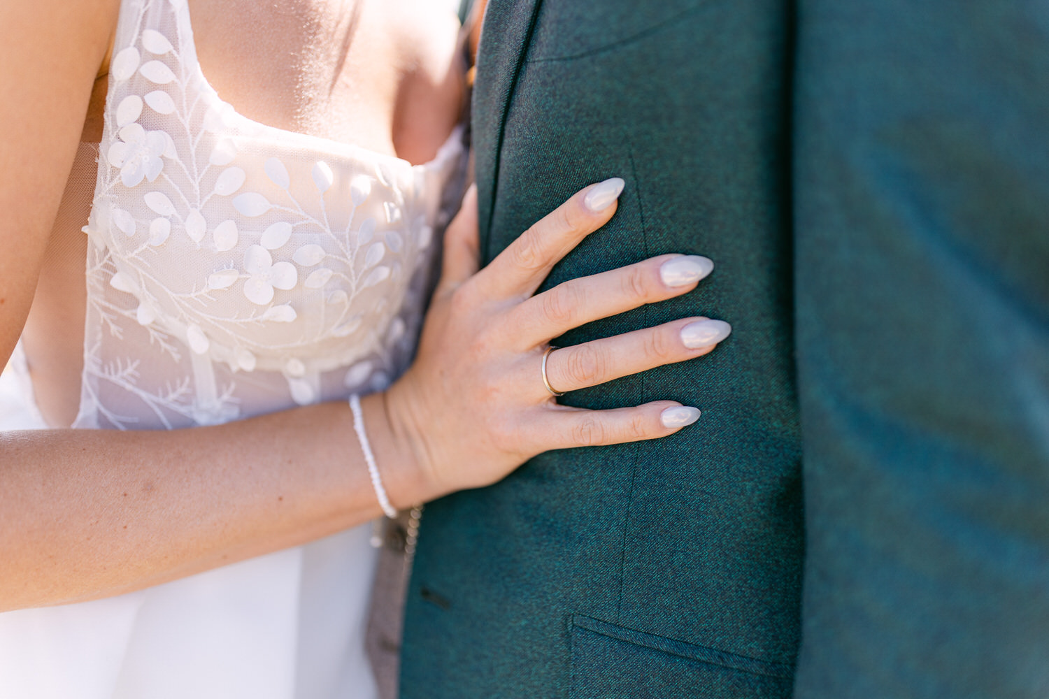 A close-up of a woman's hand resting on a man's suit, showcasing intricate floral embroidery and elegant nails.