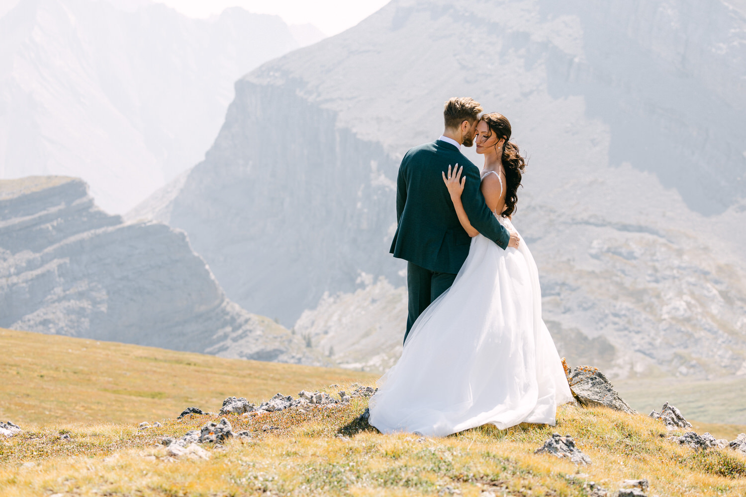 Romantic Mountain Wedding::A couple in formal wedding attire embraces in a scenic mountainous landscape, capturing a moment of love surrounded by nature.