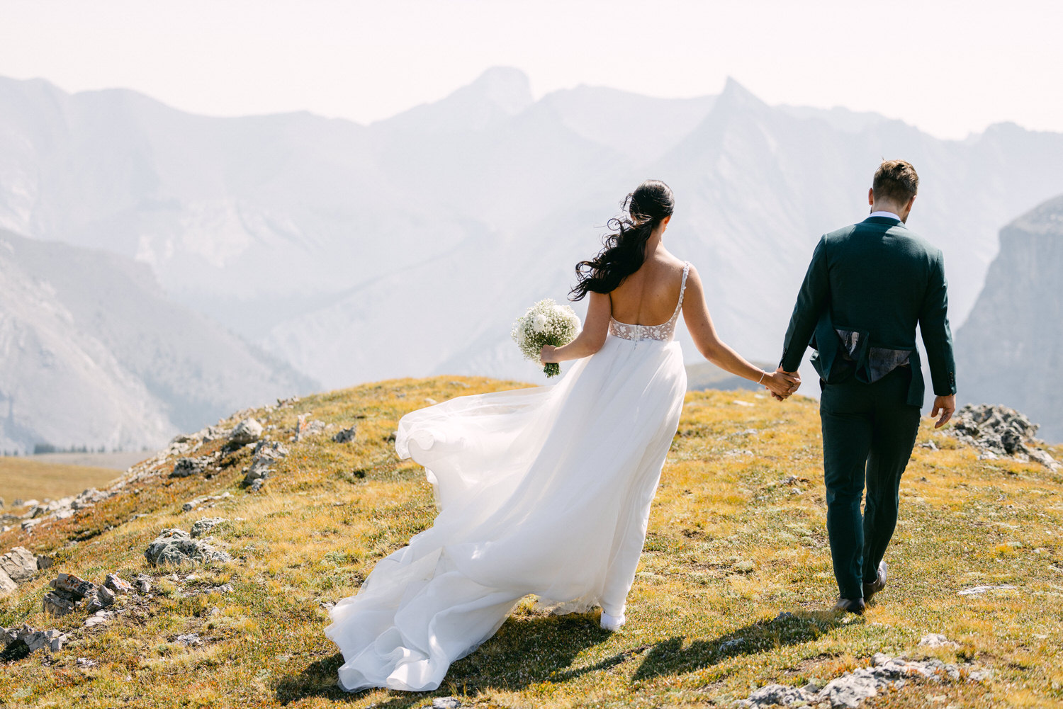 A bride and groom walk hand-in-hand through a picturesque mountain landscape, showcasing love and adventure against a stunning backdrop.