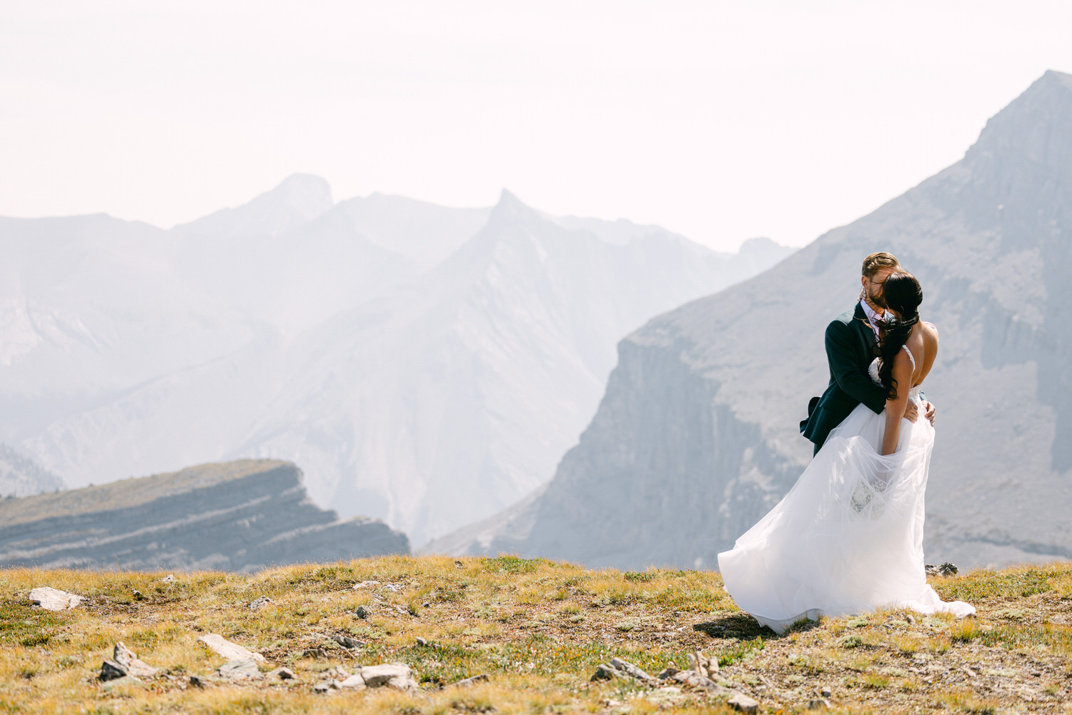 A couple embracing in wedding attire with a scenic mountain backdrop, capturing their love and joy on a special day.