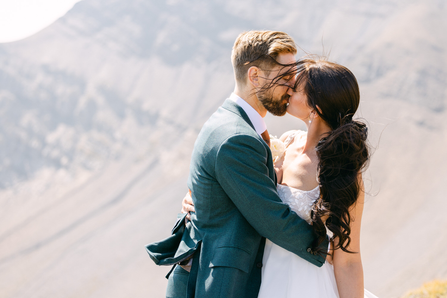 A couple embraces and shares a kiss against a stunning mountain backdrop, capturing a moment of love and joy.