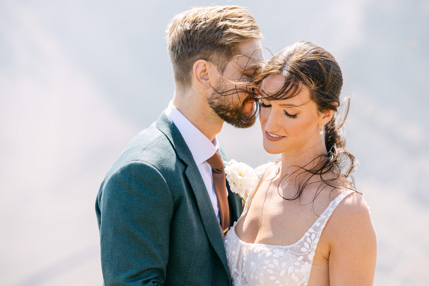 A bride and groom sharing an intimate moment outdoors, with the bride looking down lovingly and the groom leaning in closer.