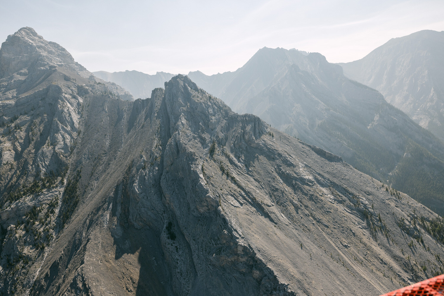 A stunning view of rugged mountain peaks and slopes under a clear sky, showcasing intricate rock formations and sparse vegetation.