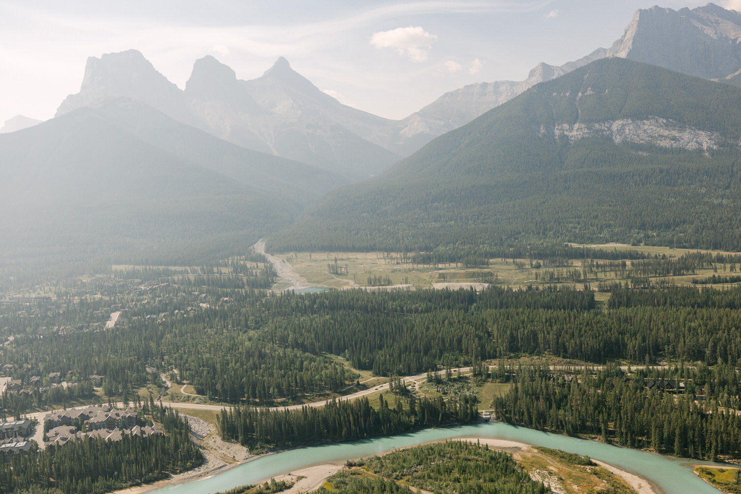 Aerial view of a lush, green valley surrounded by mountains, featuring a winding river and a small town nestled among the trees.