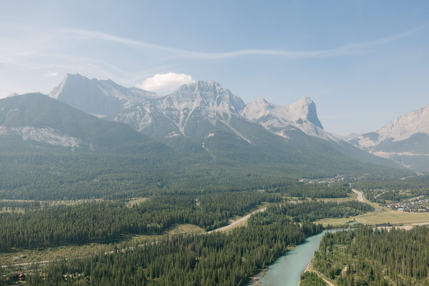 A scenic view of majestic mountains towering over a lush forest and winding river, set under a clear sky.