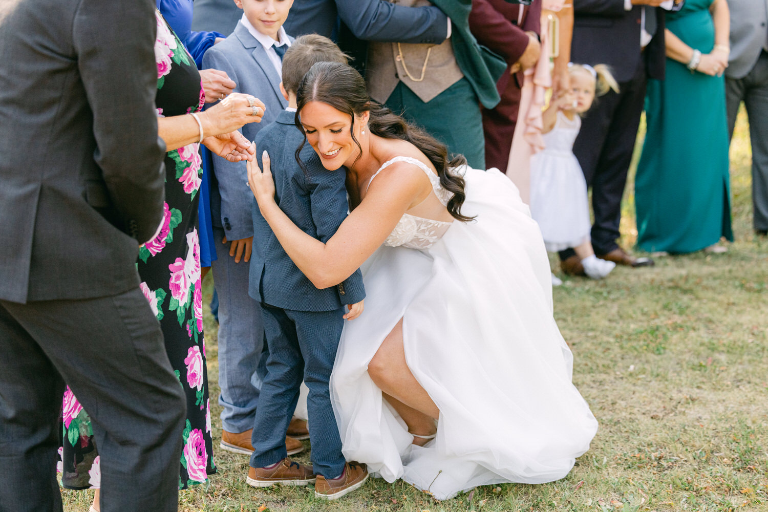 A bride interacts warmly with a young boy while surrounded by wedding guests, capturing a moment of joy during the celebration.