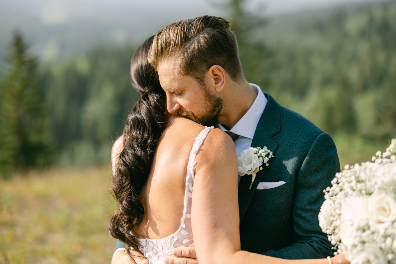 A couple shares a tender moment in a scenic outdoor setting, with the groom resting his face on the bride's shoulder, highlighting their connection and love.