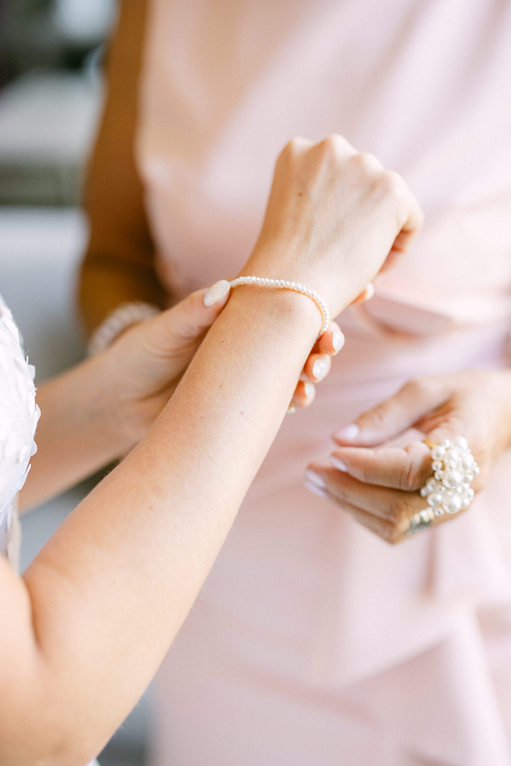 Two women exchanging a delicate pearl bracelet in an elegant setting.