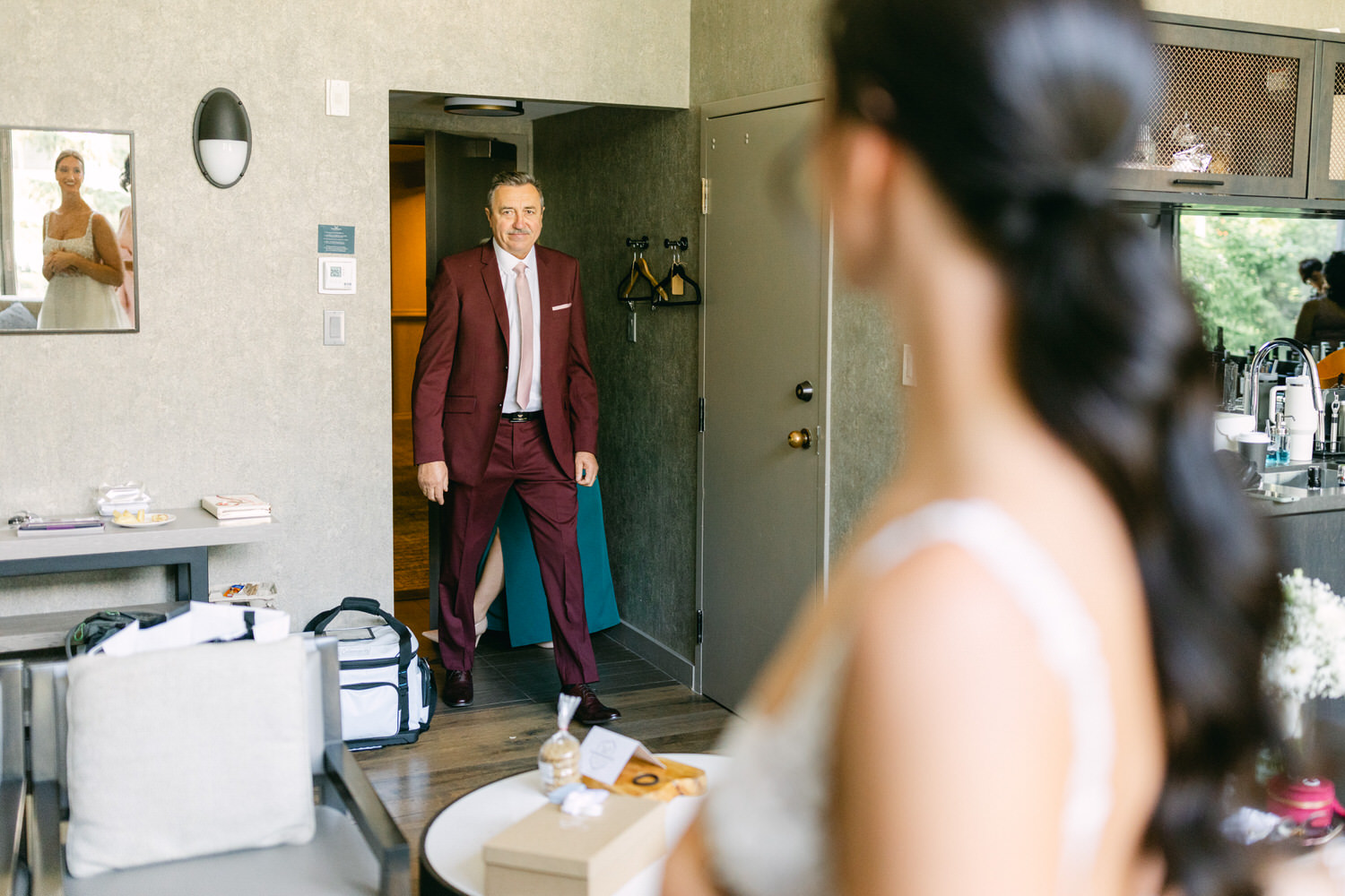 A man in a maroon suit enters the room, surprised to see a woman in a wedding dress reflecting in the mirror.