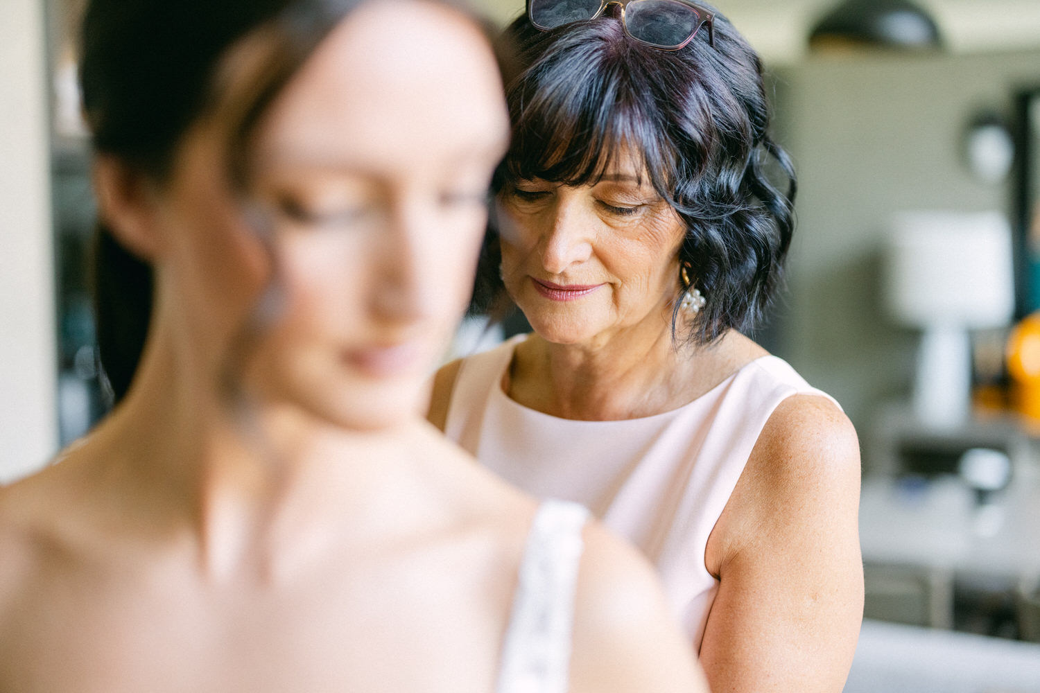 A mother helps her daughter prepare for a special occasion, showcasing intimacy and connection in a soft-focused setting.