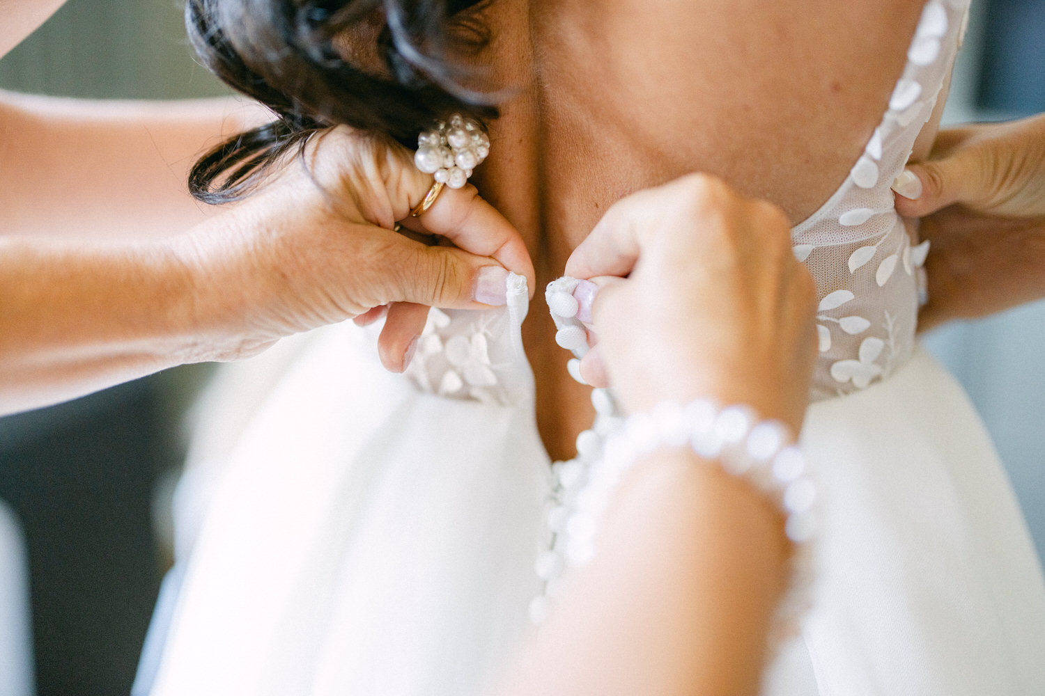 A close-up of hands adjusting a wedding dress, showcasing detailed floral lace and a delicate back design.