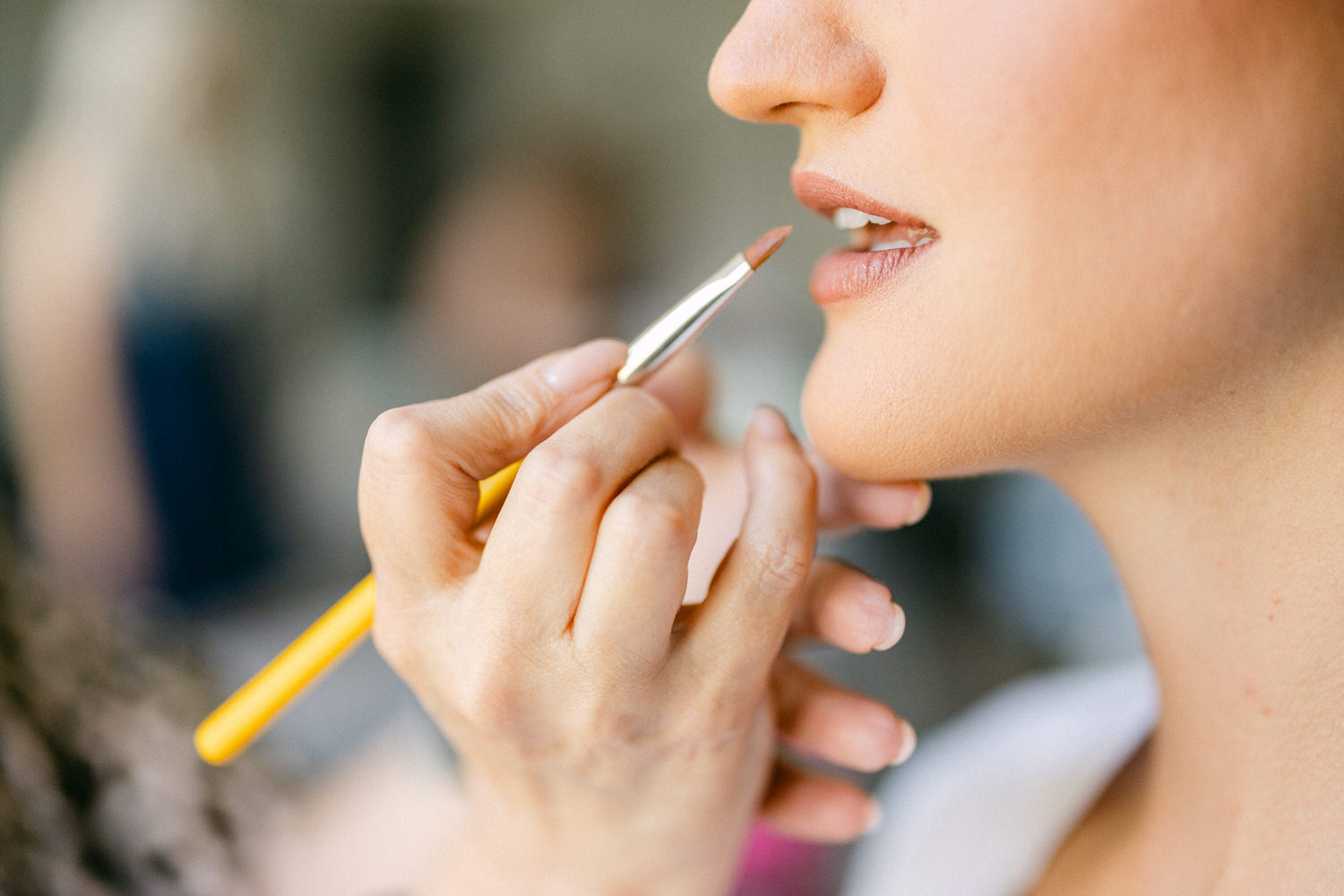 Close-up of a makeup artist applying lip color to a model's lips with a brush.