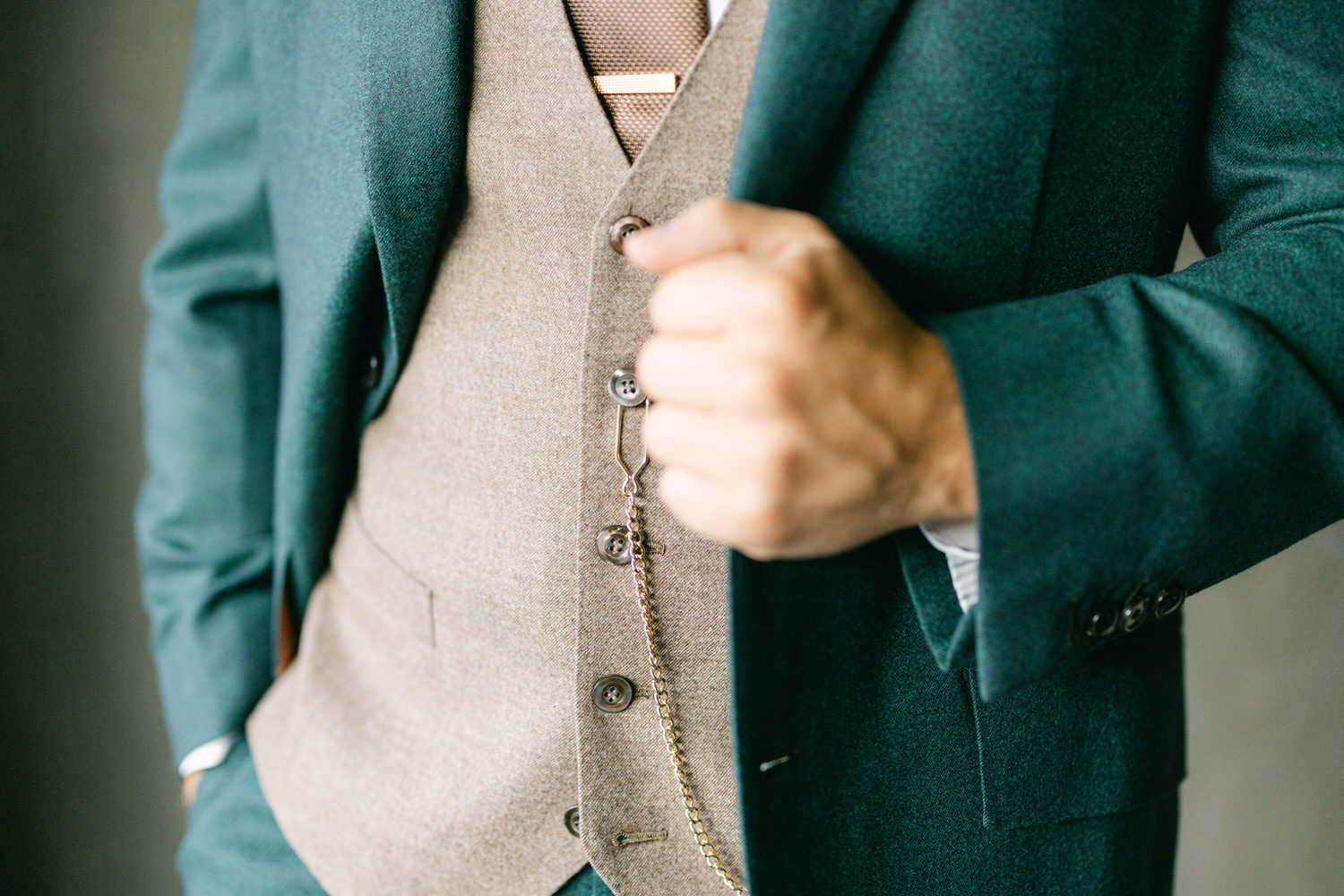 Close-up of a well-tailored suit featuring a green blazer and a brown vest, showcasing stylish buttons and accessories.