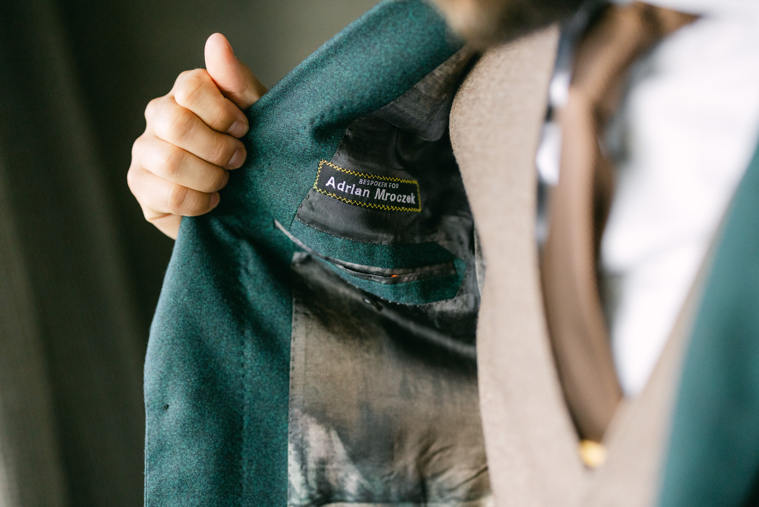 Close-up of a bespoke suit jacket with a visible label reading "Bespoken for Adrian Mroczek," highlighting the craftsmanship and personalization.