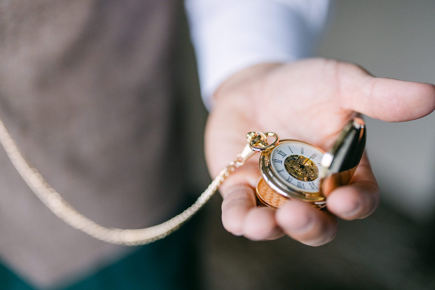 A vintage pocket watch held in a person's hand, displaying intricate details and a gold chain.