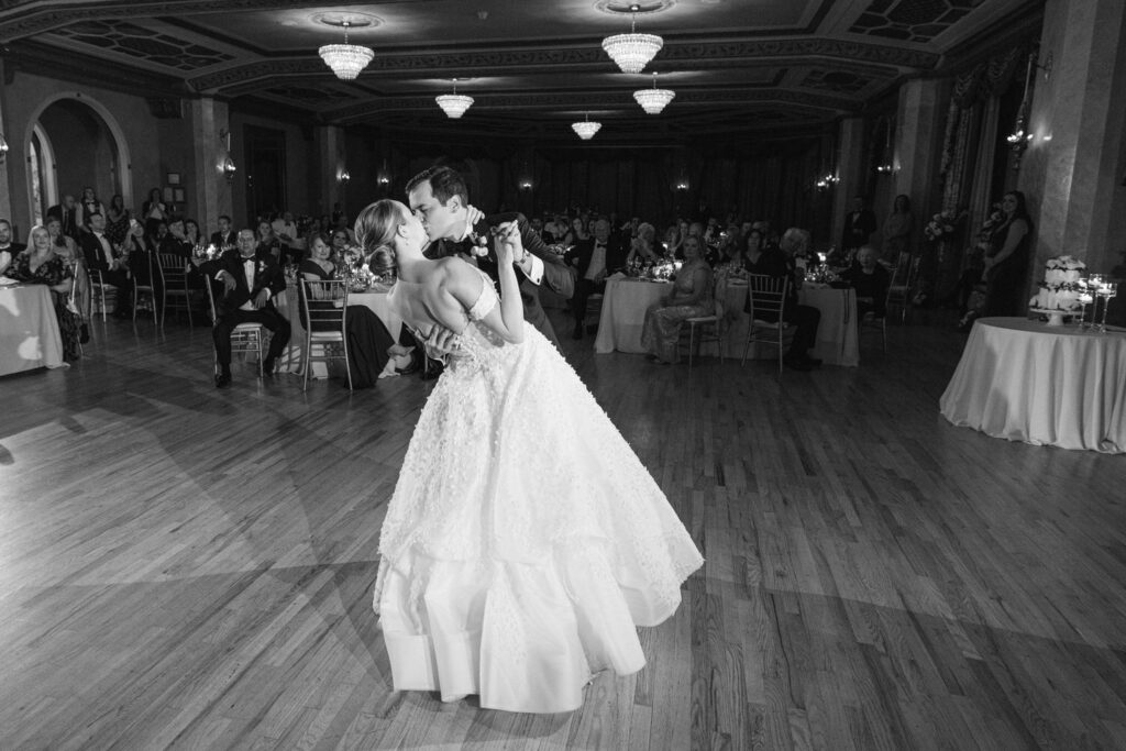 A couple shares a tender moment during their first dance at a wedding reception, surrounded by guests in a beautifully decorated venue.