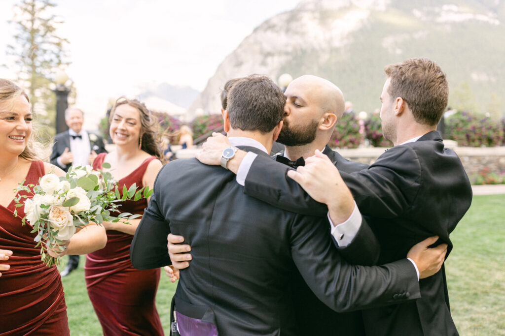 A joyful moment captured with guests in formal attire embracing and sharing laughter at a picturesque outdoor wedding venue, surrounded by nature.