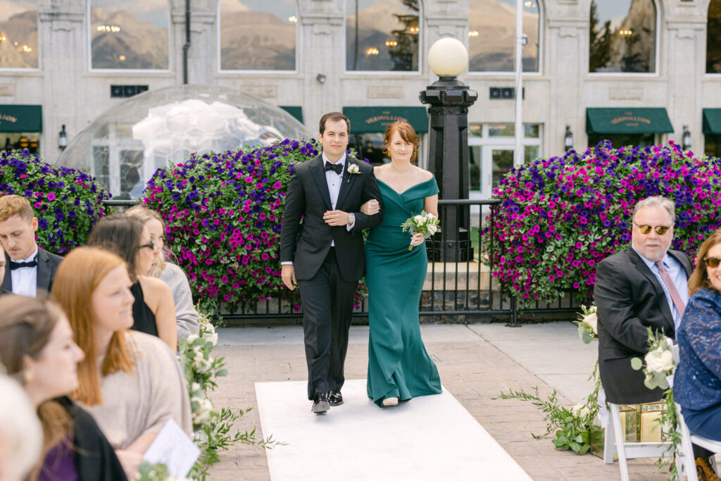 A couple walking down the aisle during a wedding ceremony, surrounded by colorful flower arrangements and seated guests.