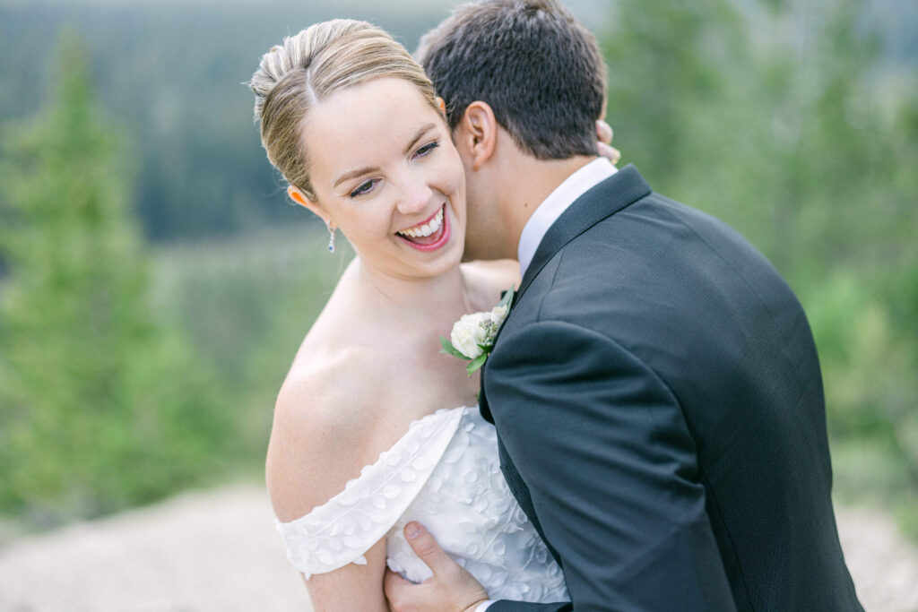 A radiant bride laughs as her partner embraces her, surrounded by a beautiful natural backdrop.