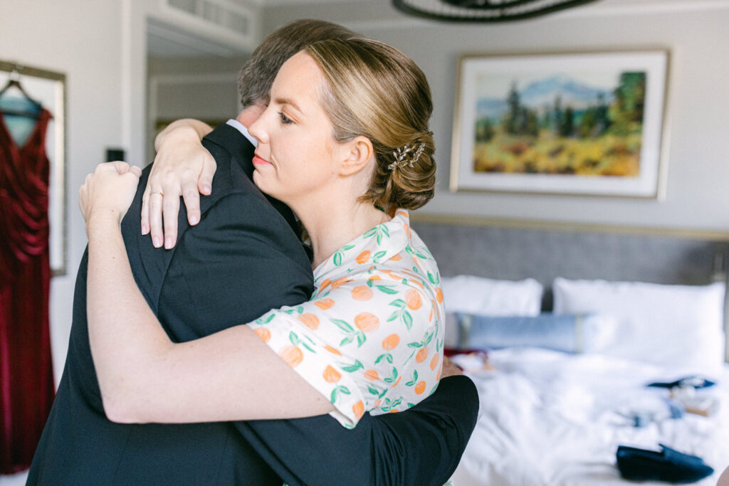 A woman in a floral shirt embraces a man in a suit, both conveying a heartfelt moment in an elegantly decorated hotel room.