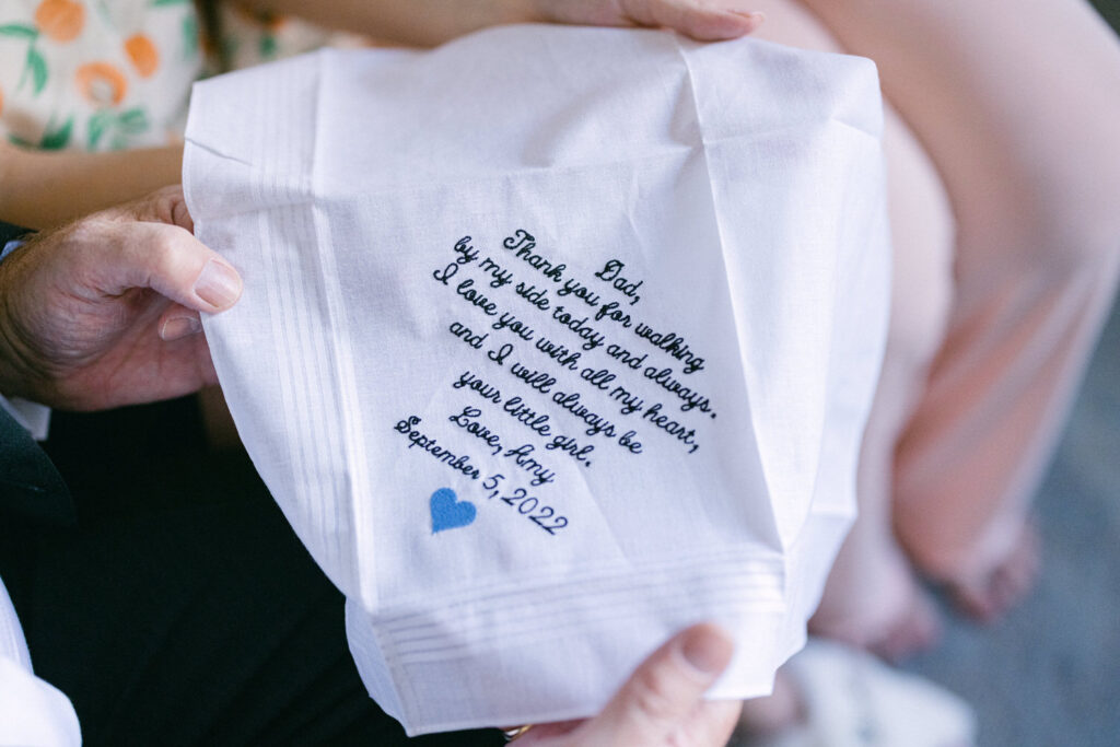 A close-up of a white handkerchief embroidered with a heartfelt message from a daughter to her father, expressing love and gratitude, dated September 5, 2022.