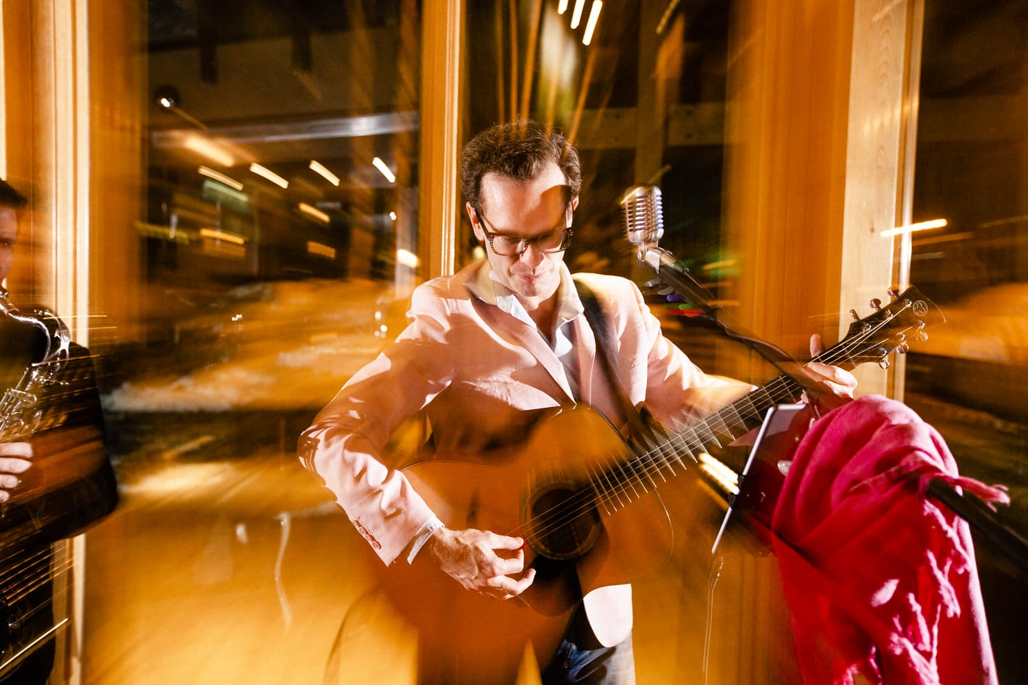 Musician in a white jacket passionately playing guitar on stage, with vibrant lights creating a dynamic, blurred background effect.