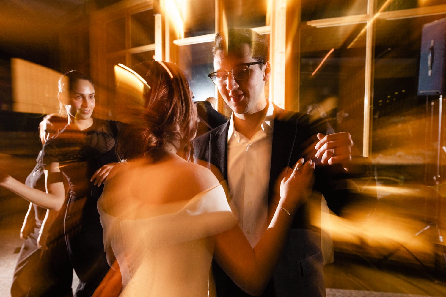 A lively dance scene with a woman in a white dress and a man in a black suit, surrounded by blurred figures and vibrant lighting effects.