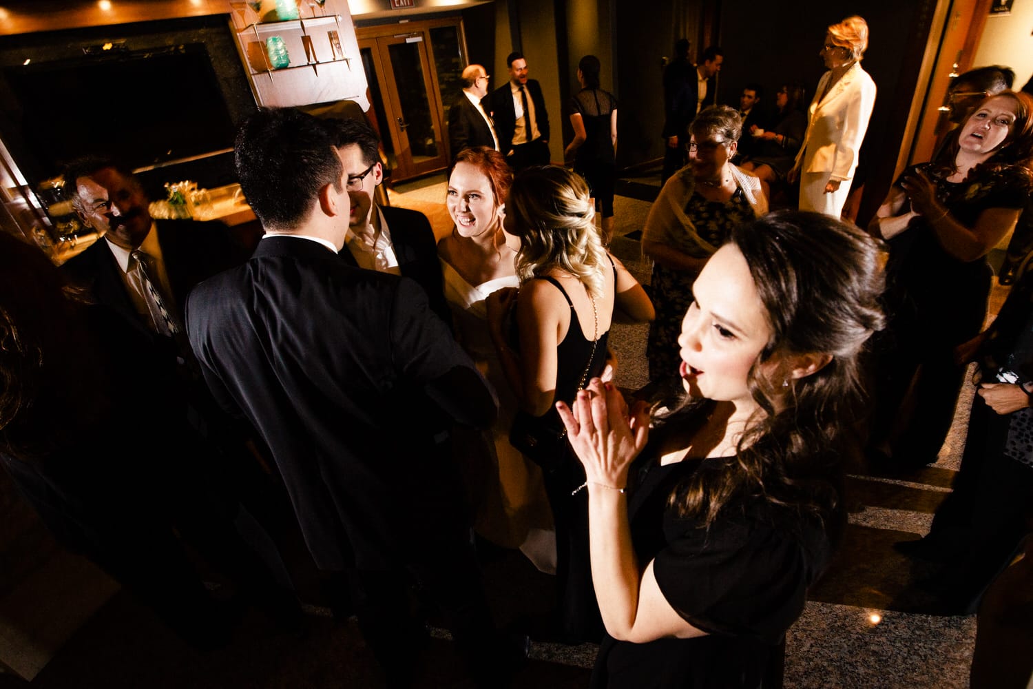 A lively group of elegantly dressed people engaging in conversation and celebration at a social event.