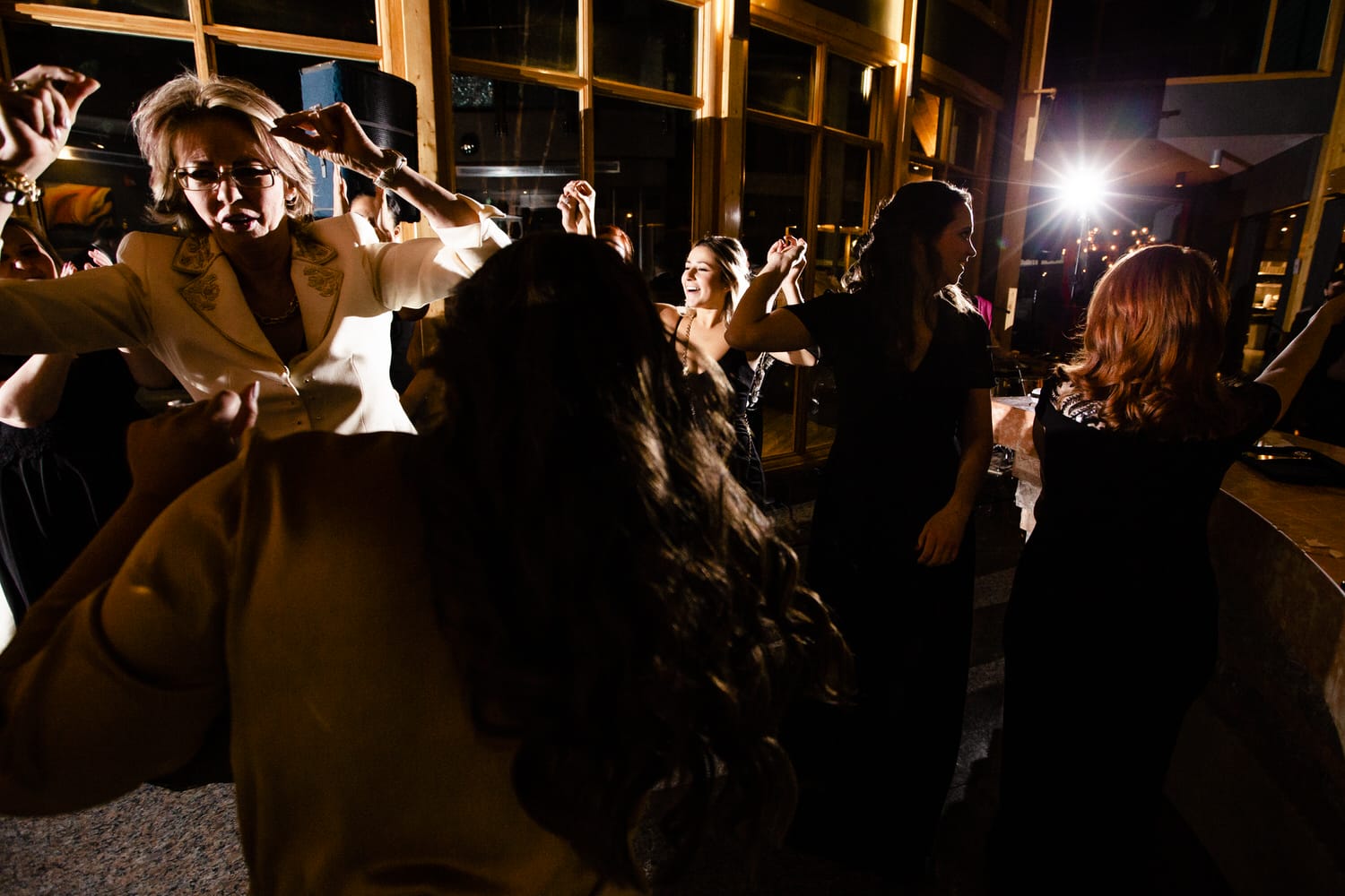 A group of women dancing joyfully at a nighttime celebration, with vibrant lighting and a lively atmosphere.