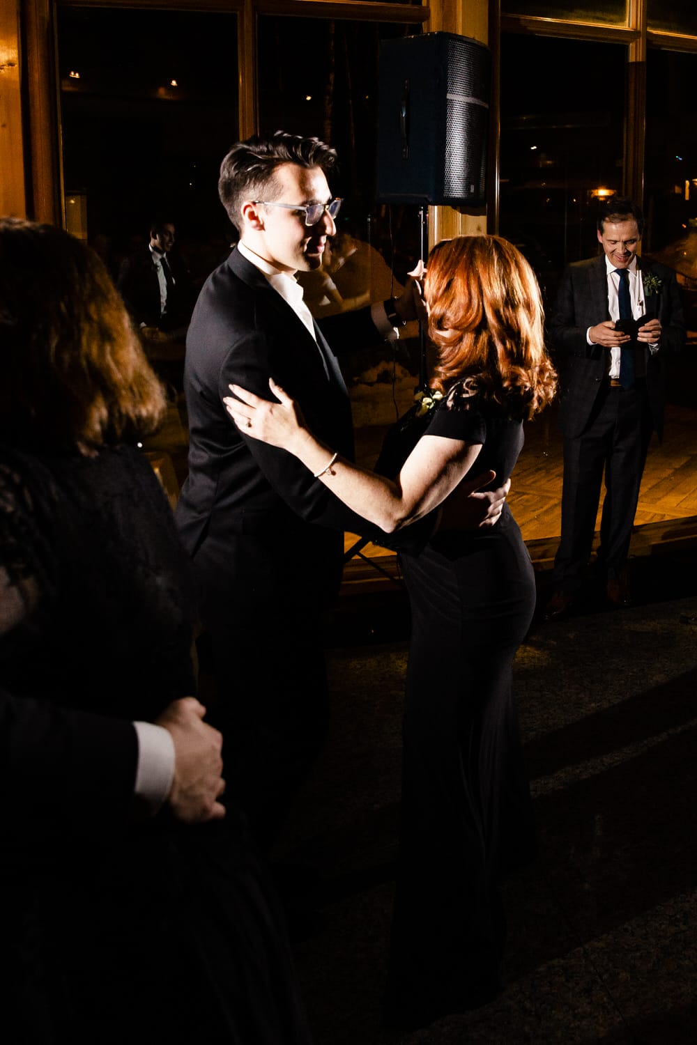 Dancing Under the Stars::A couple shares a dance in an elegantly lit venue during an evening celebration, with guests in the background.