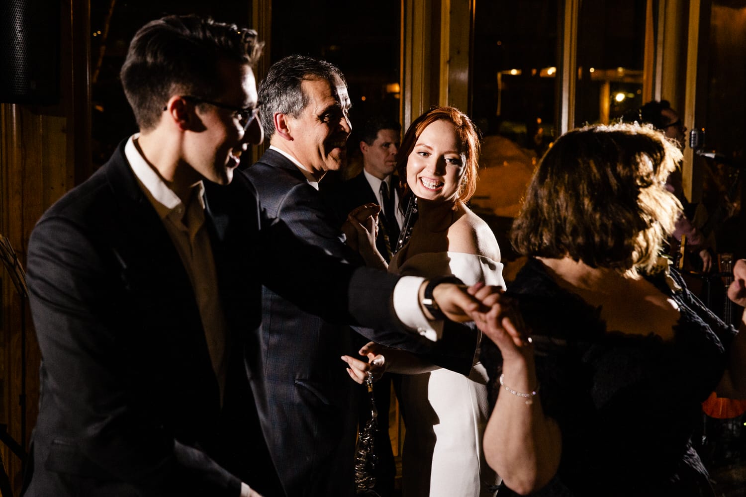 Group of people dancing joyfully at a festivity, illuminated by warm lighting.