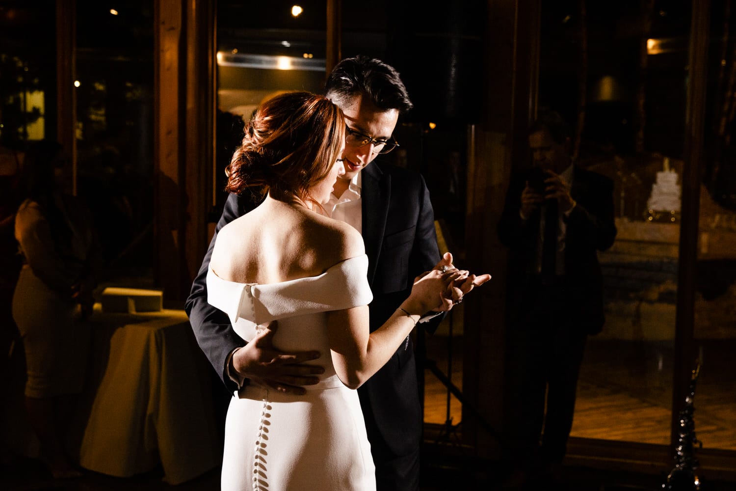 A bride and groom share a tender moment dancing together at their wedding reception, surrounded by soft lighting and reflections.