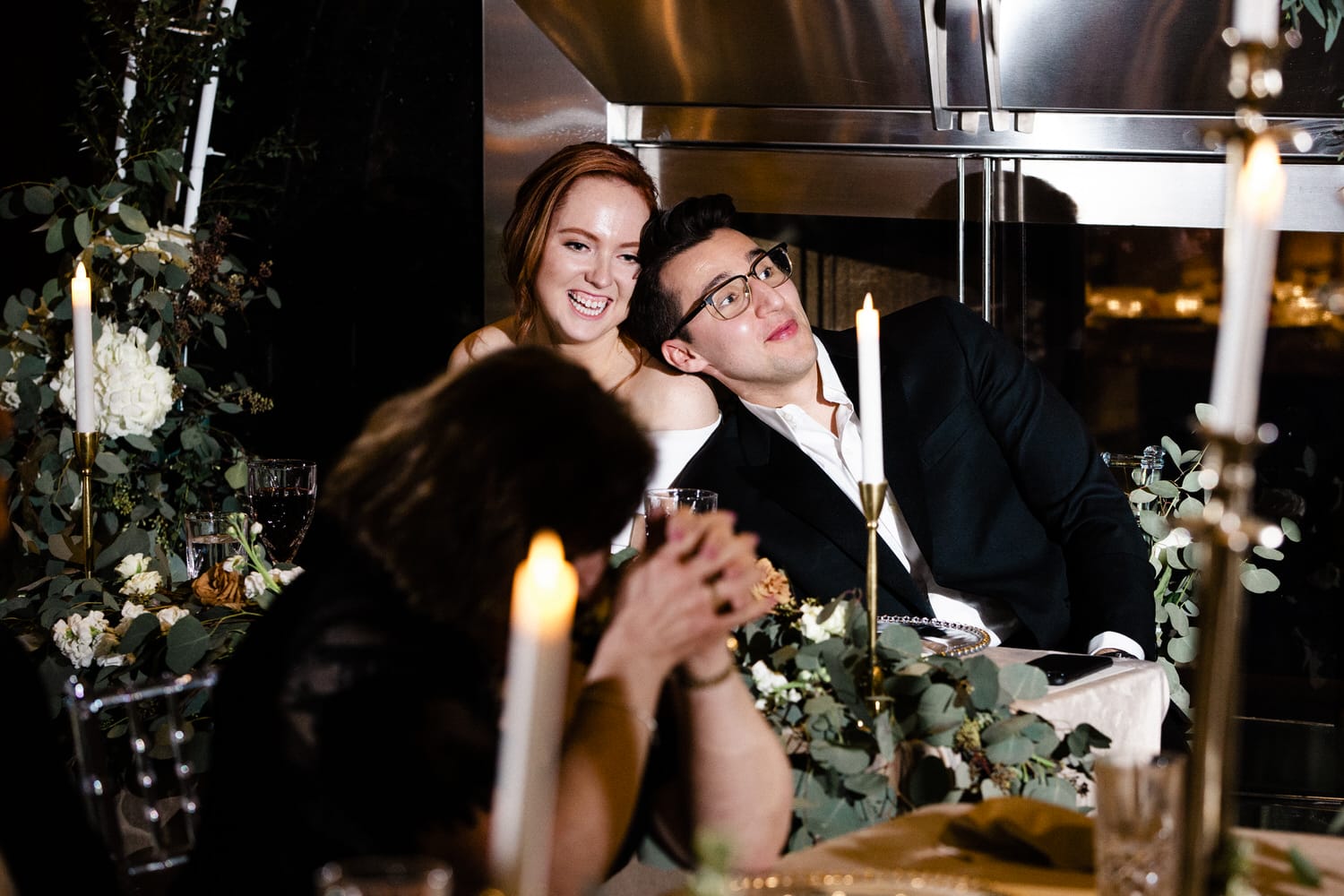 A couple shares a warm moment at a beautifully decorated dinner table, surrounded by candlelight and floral arrangements.