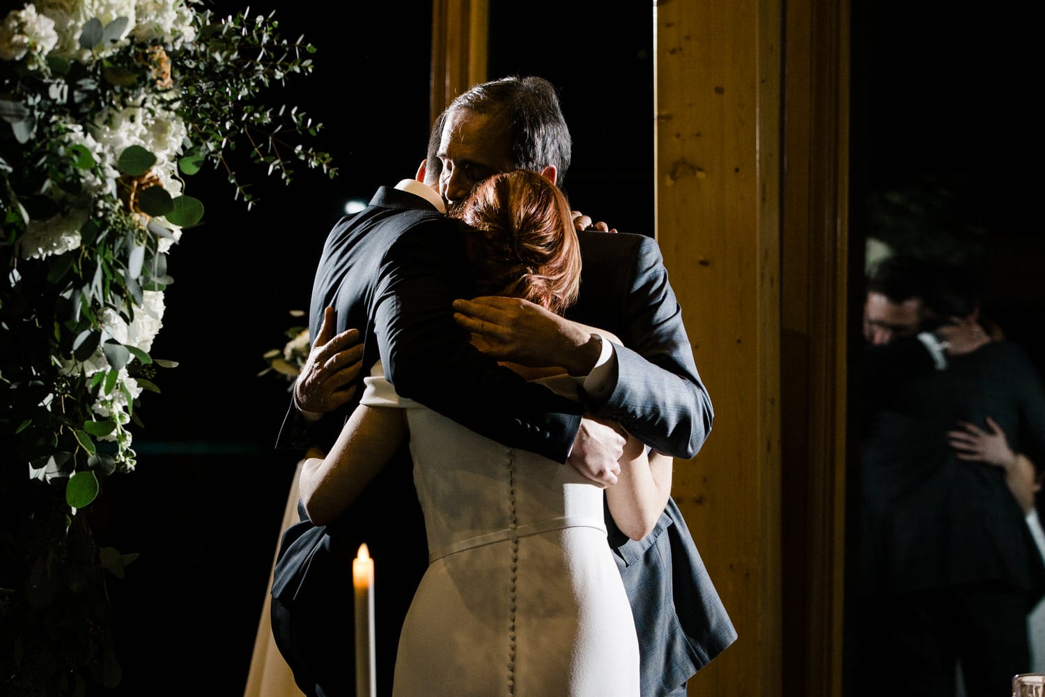 A heartfelt moment as a bride and groom embrace during their wedding ceremony, surrounded by floral decorations and soft candlelight.