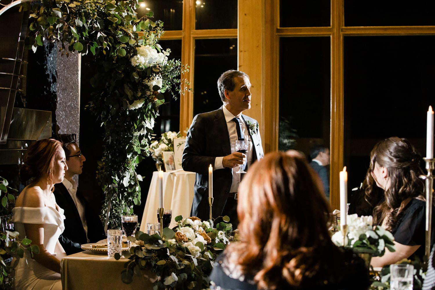 A man gives a heartfelt toast at a beautifully decorated wedding reception, surrounded by guests enjoying the moment.