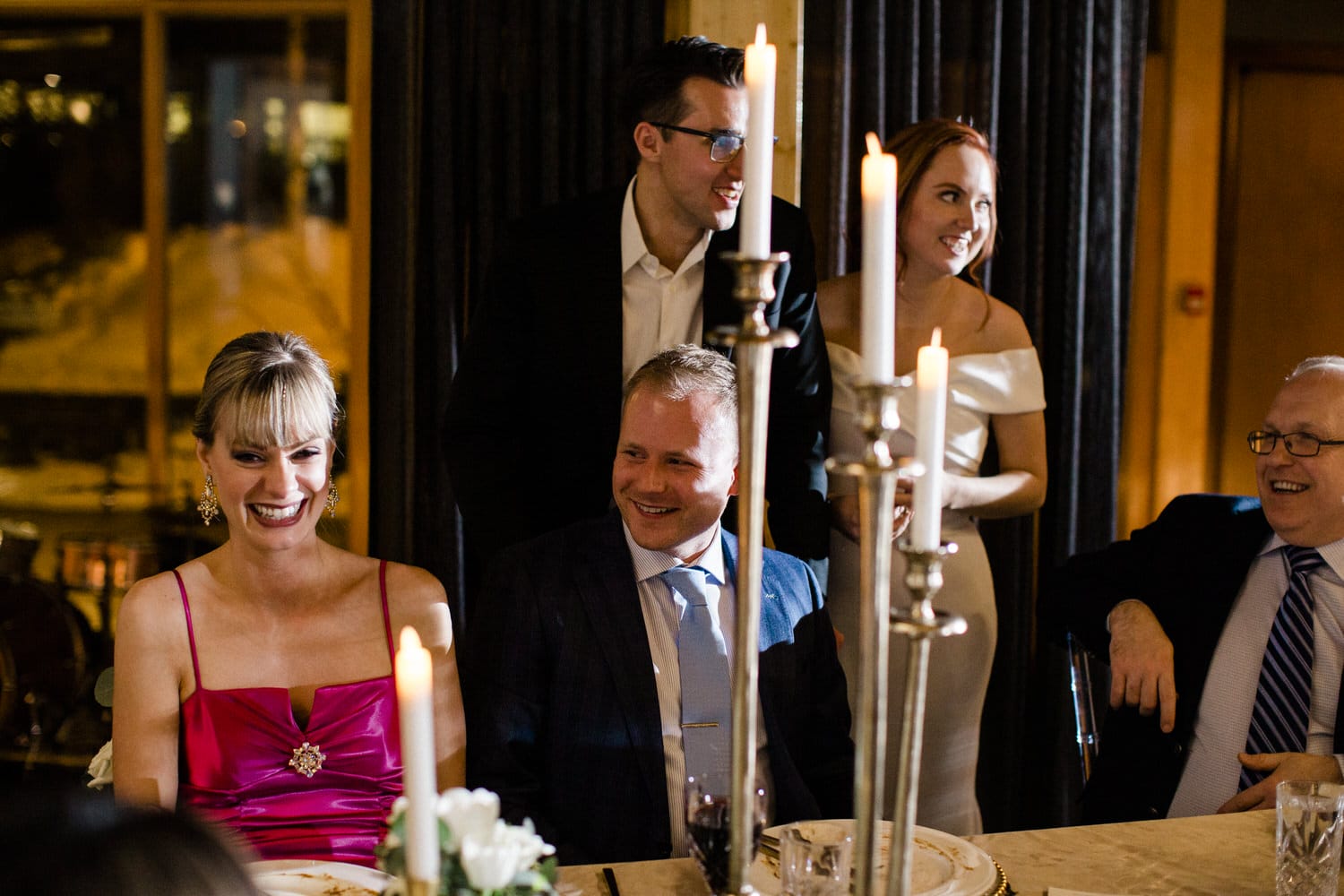 A group of elegantly dressed individuals enjoying a joyous moment at a dinner table, with candles and flowers creating a warm ambiance.