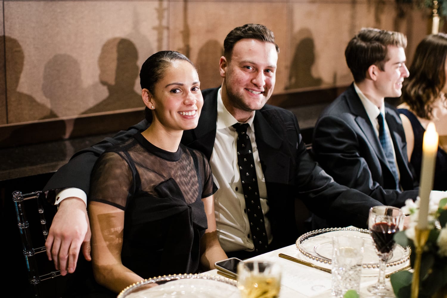 A smiling couple enjoying a refined dining experience with friends at a beautifully set table.