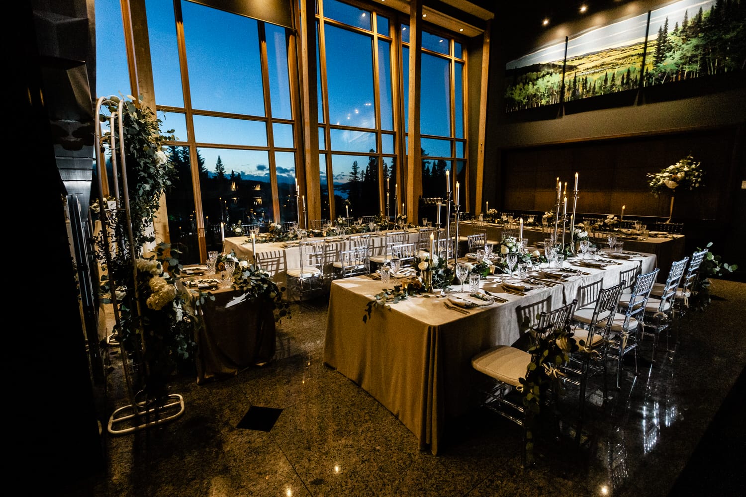 A beautifully set dining room with candlelit tables, large windows showcasing a twilight view, and elegant floral arrangements.