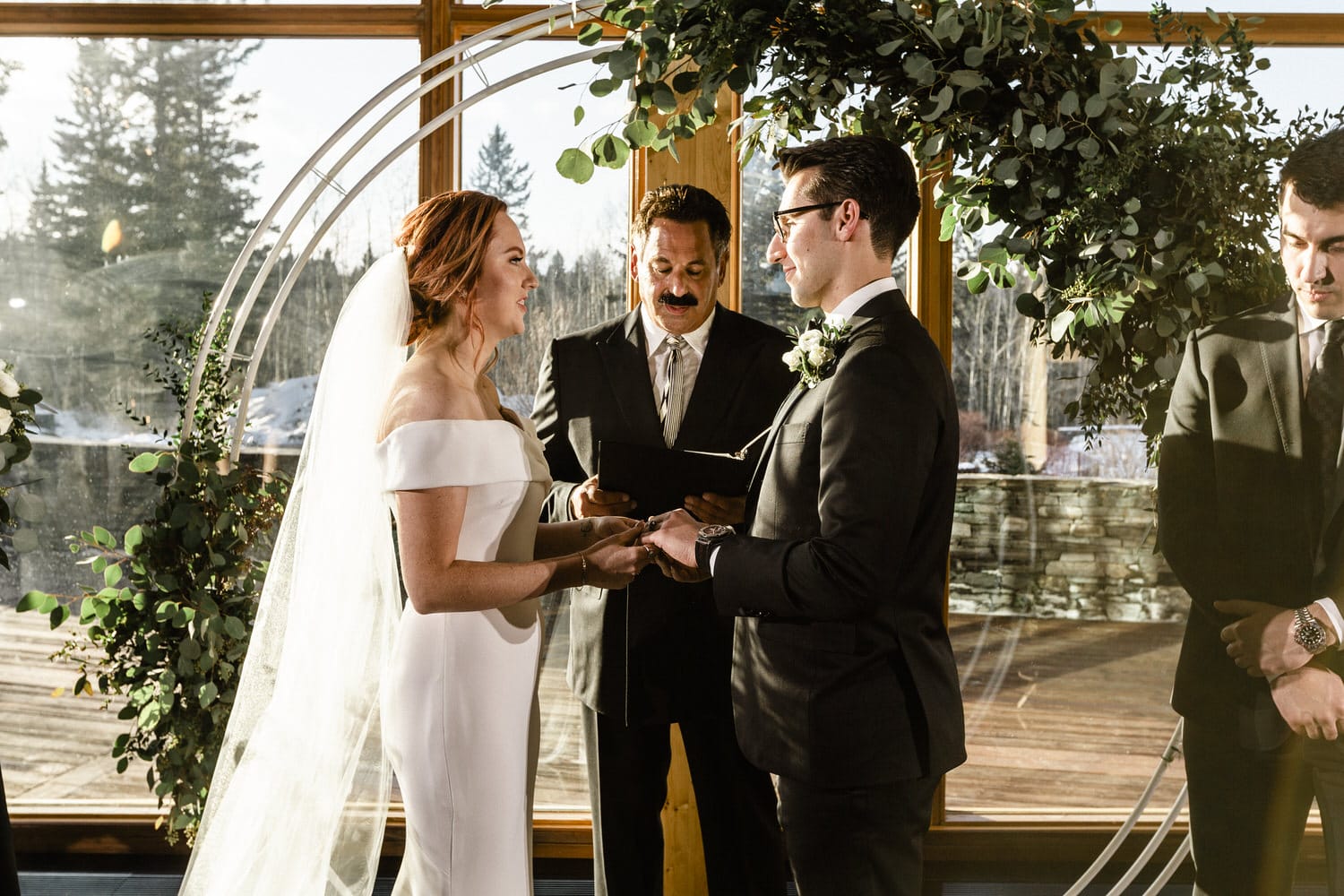 A couple exchanging vows during their wedding ceremony, surrounded by greenery and a celebrant.