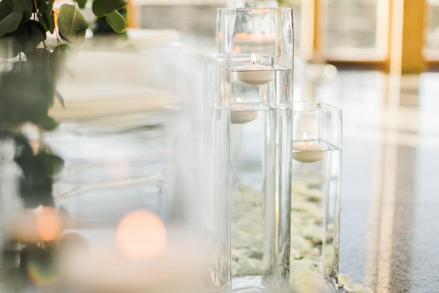 Clear glass candle holders with floating candles, surrounded by rose petals and greenery, creating a serene ambiance.