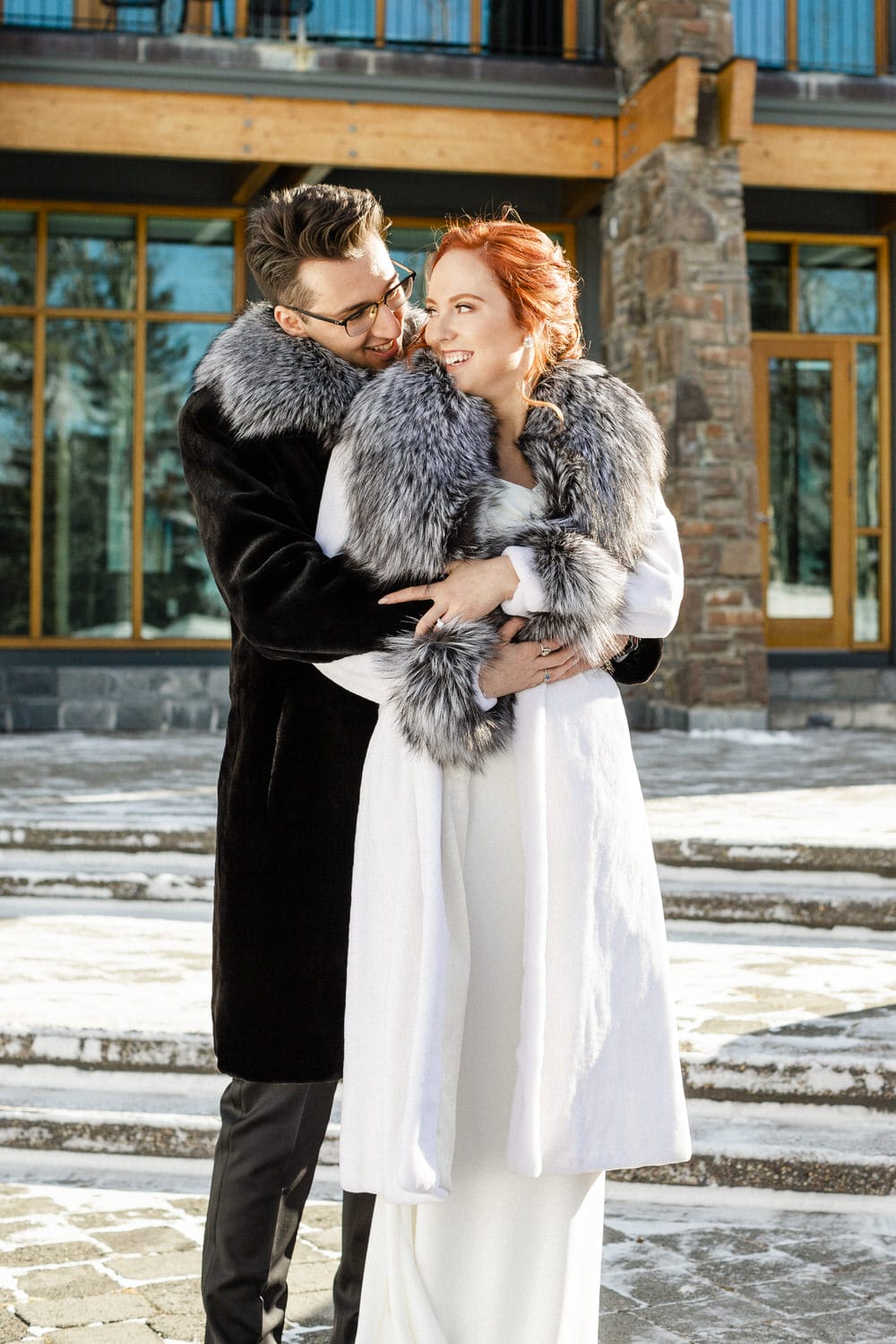 A couple in stylish winter attire sharing a joyful moment outdoors in a snowy setting.