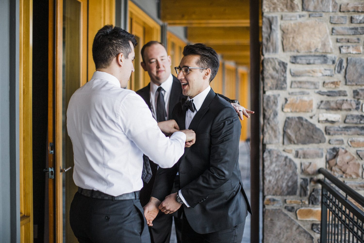 Friends adjusting the groom's attire and sharing laughter before the ceremony.